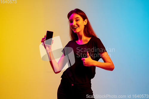 Image of Young caucasian woman\'s portrait on gradient blue-yellow studio background in neon light