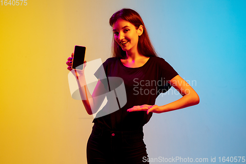 Image of Young caucasian woman\'s portrait on gradient blue-yellow studio background in neon light