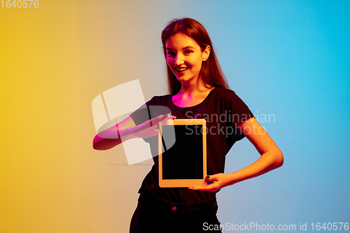 Image of Young caucasian woman\'s portrait on gradient blue-yellow studio background in neon light