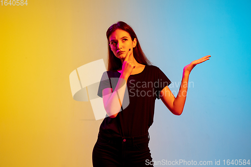 Image of Young caucasian woman\'s portrait on gradient blue-yellow studio background in neon light