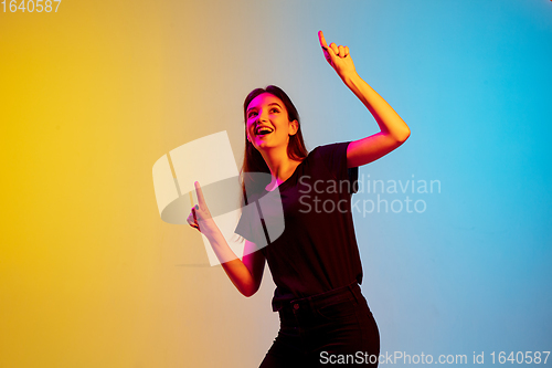 Image of Young caucasian woman\'s portrait on gradient blue-yellow studio background in neon light