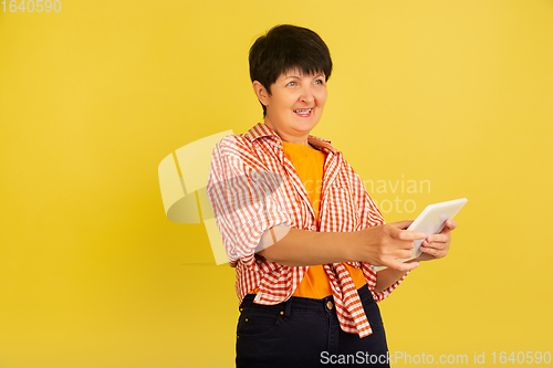 Image of Senior woman isolated on yellow background. Tech and joyful elderly lifestyle concept