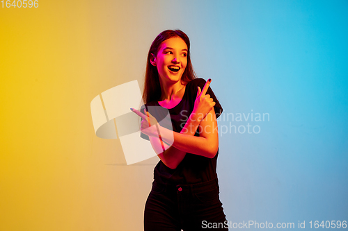 Image of Young caucasian woman\'s portrait on gradient blue-yellow studio background in neon light