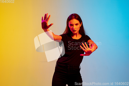 Image of Young caucasian woman\'s portrait on gradient blue-yellow studio background in neon light