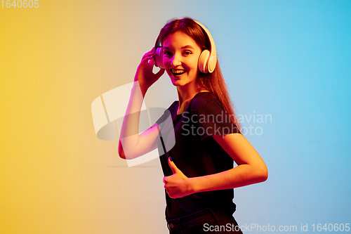 Image of Young caucasian woman\'s portrait on gradient blue-yellow studio background in neon light