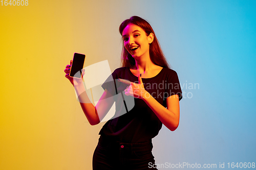 Image of Young caucasian woman\'s portrait on gradient blue-yellow studio background in neon light