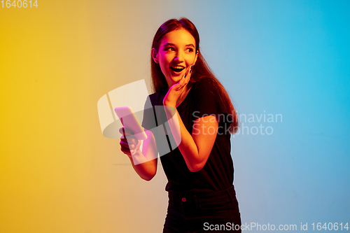 Image of Young caucasian woman\'s portrait on gradient blue-yellow studio background in neon light