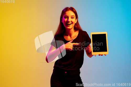 Image of Young caucasian woman\'s portrait on gradient blue-yellow studio background in neon light