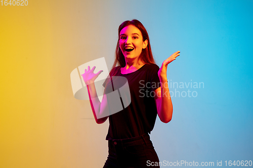 Image of Young caucasian woman\'s portrait on gradient blue-yellow studio background in neon light