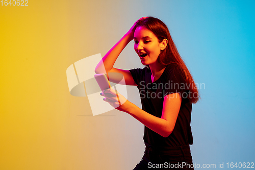 Image of Young caucasian woman\'s portrait on gradient blue-yellow studio background in neon light