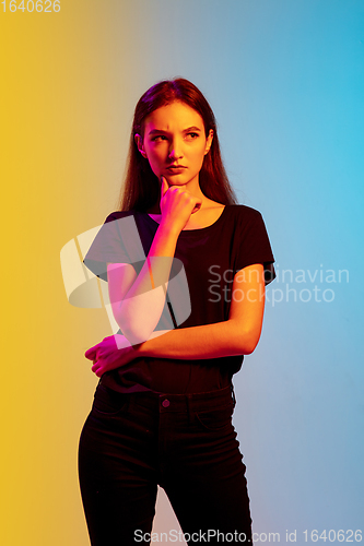 Image of Young caucasian woman\'s portrait on gradient blue-yellow studio background in neon light