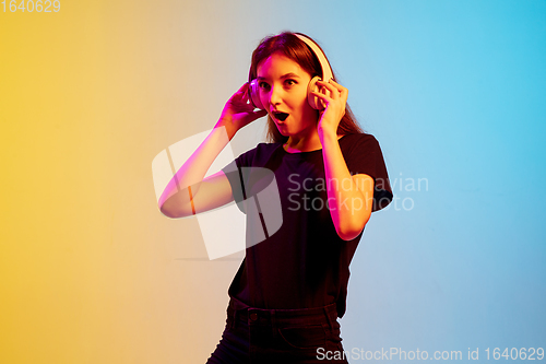 Image of Young caucasian woman\'s portrait on gradient blue-yellow studio background in neon light