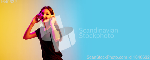 Image of Young caucasian woman\'s portrait on gradient blue-yellow studio background in neon light
