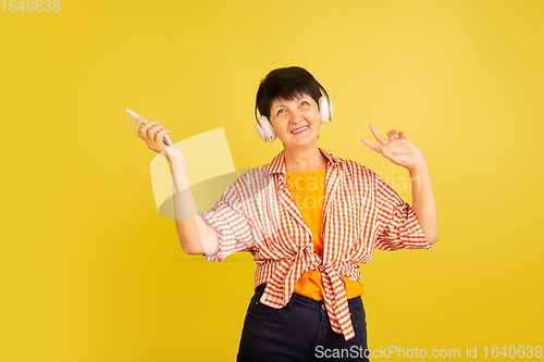 Image of Senior woman isolated on yellow background. Tech and joyful elderly lifestyle concept