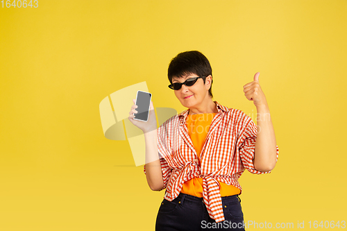 Image of Senior woman isolated on yellow background. Tech and joyful elderly lifestyle concept