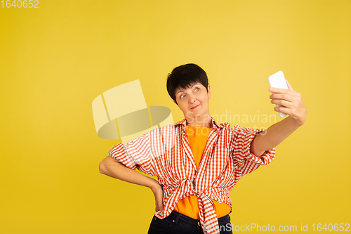 Image of Senior woman isolated on yellow background. Tech and joyful elderly lifestyle concept