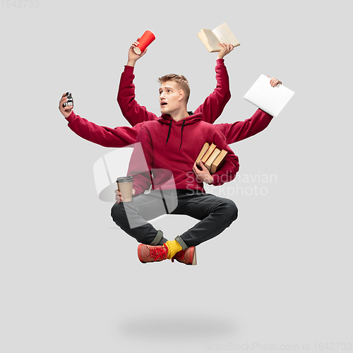 Image of Handsome multi-armed student levitating isolated on grey studio background with equipment