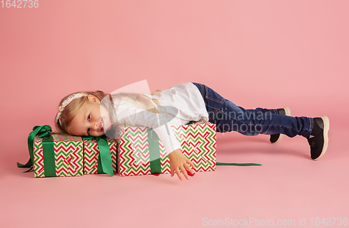 Image of Giving and getting presents on Christmas holidays. Little smiling girl having fun isolated on pink studio background