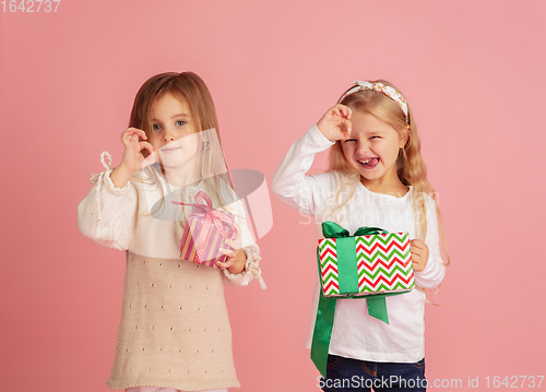 Image of Giving and getting presents on Christmas holidays. Two little smiling children having fun isolated on pink studio background