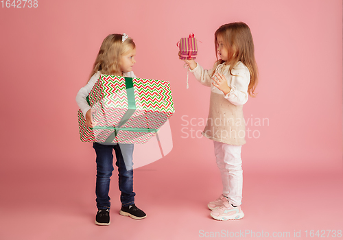 Image of Giving and getting presents on Christmas holidays. Two little smiling children having fun isolated on pink studio background