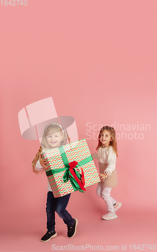 Image of Giving and getting presents on Christmas holidays. Two little smiling children having fun isolated on pink studio background