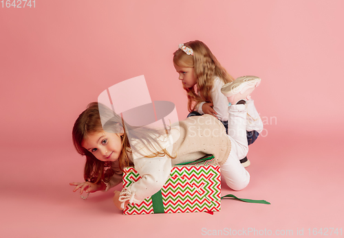 Image of Giving and getting presents on Christmas holidays. Two little smiling children having fun isolated on pink studio background