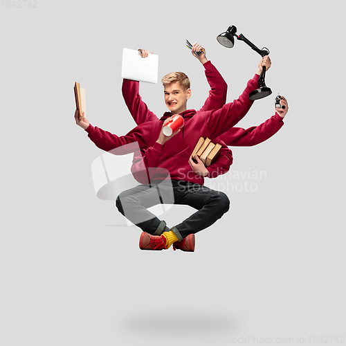 Image of Handsome multi-armed student levitating isolated on grey studio background with equipment