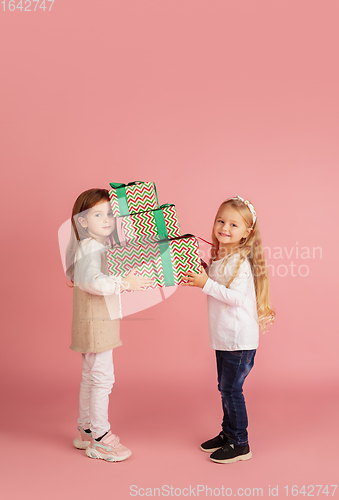 Image of Giving and getting presents on Christmas holidays. Two little smiling children having fun isolated on pink studio background