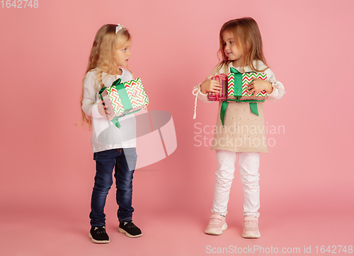 Image of Giving and getting presents on Christmas holidays. Two little smiling children having fun isolated on pink studio background