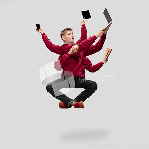 Image of Handsome multi-armed student levitating isolated on grey studio background with equipment