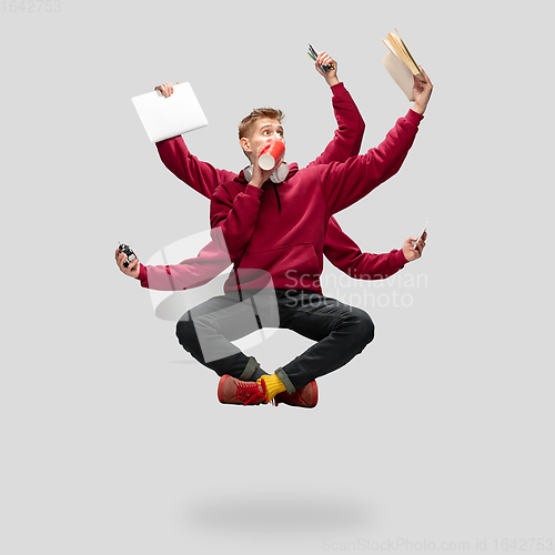 Image of Handsome multi-armed student levitating isolated on grey studio background with equipment