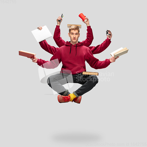 Image of Handsome multi-armed student levitating isolated on grey studio background with equipment