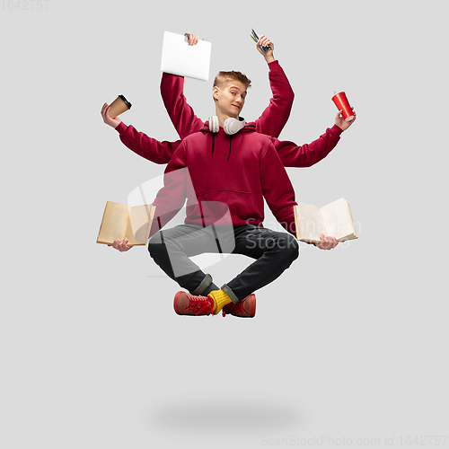 Image of Handsome multi-armed student levitating isolated on grey studio background with equipment