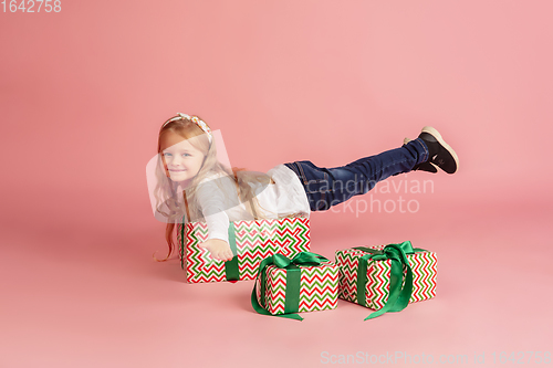 Image of Giving and getting presents on Christmas holidays. Little smiling girl having fun isolated on pink studio background