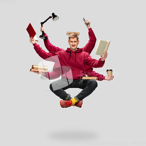 Image of Handsome multi-armed student levitating isolated on grey studio background with equipment