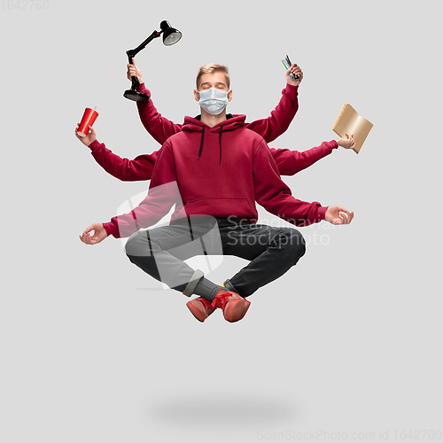 Image of Handsome multi-armed student levitating isolated on grey studio background with equipment