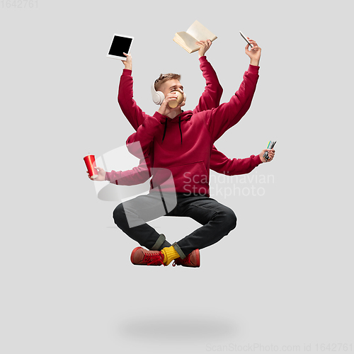 Image of Handsome multi-armed student levitating isolated on grey studio background with equipment