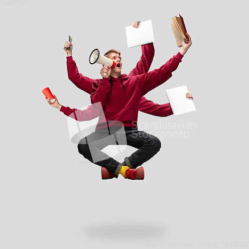 Image of Handsome multi-armed student levitating isolated on grey studio background with equipment