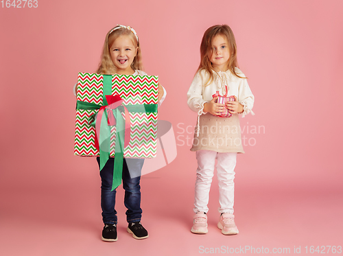 Image of Giving and getting presents on Christmas holidays. Two little smiling children having fun isolated on pink studio background