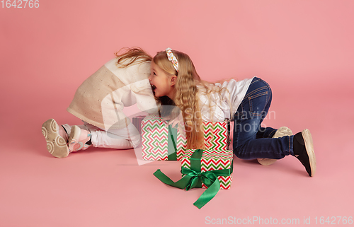 Image of Giving and getting presents on Christmas holidays. Two little smiling children having fun isolated on pink studio background