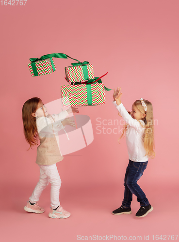 Image of Giving and getting presents on Christmas holidays. Two little smiling children having fun isolated on pink studio background