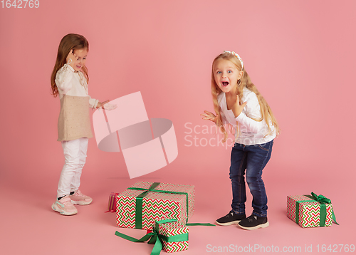 Image of Giving and getting presents on Christmas holidays. Two little smiling children having fun isolated on pink studio background