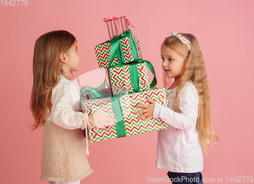 Image of Giving and getting presents on Christmas holidays. Two little smiling children having fun isolated on pink studio background