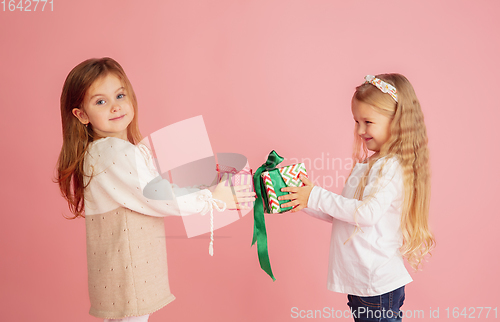 Image of Giving and getting presents on Christmas holidays. Two little smiling children having fun isolated on pink studio background