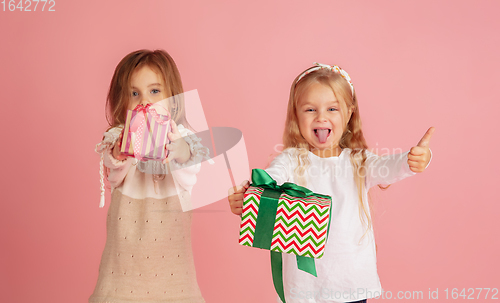 Image of Giving and getting presents on Christmas holidays. Two little smiling children having fun isolated on pink studio background