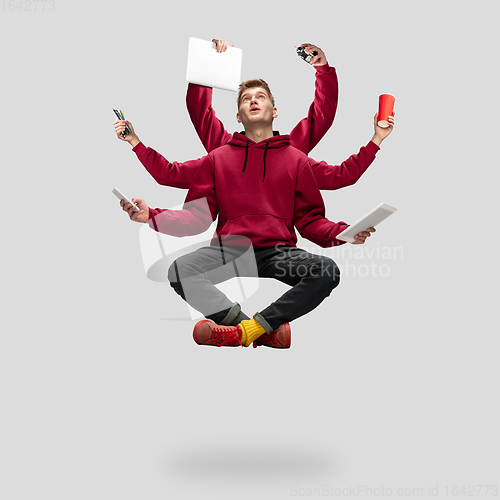 Image of Handsome multi-armed student levitating isolated on grey studio background with equipment