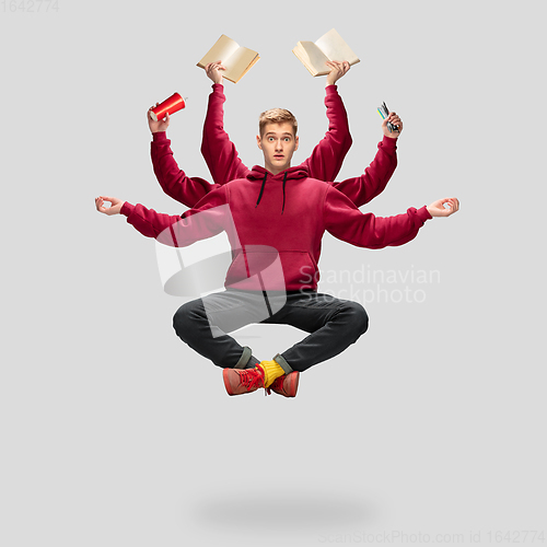 Image of Handsome multi-armed student levitating isolated on grey studio background with equipment