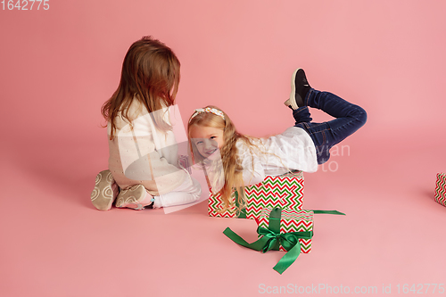 Image of Giving and getting presents on Christmas holidays. Two little smiling children having fun isolated on pink studio background