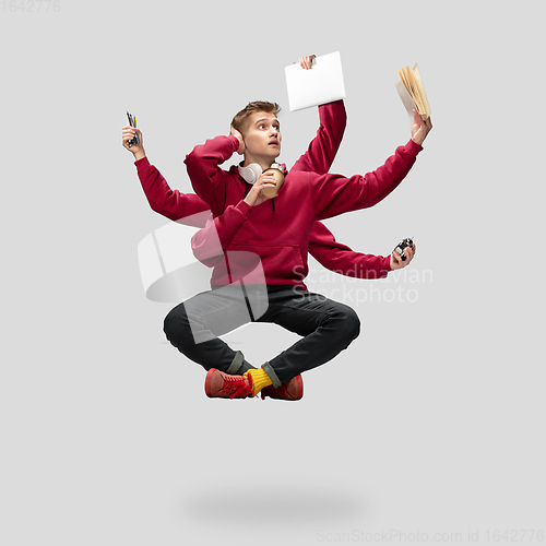 Image of Handsome multi-armed student levitating isolated on grey studio background with equipment