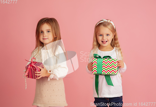 Image of Giving and getting presents on Christmas holidays. Two little smiling children having fun isolated on pink studio background